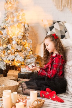 Bir kız Noel ağacı süslüyor. Yeni yıl için hazırlık yapıyorum. Kırmızı kıyafetler giyiyor ve saçında bir fiyonk var..