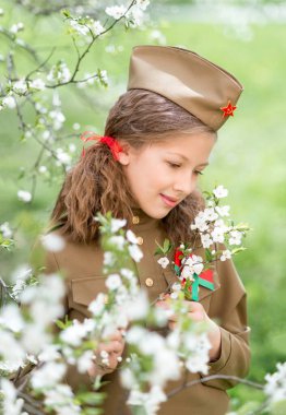 9 Mayıs Zafer Günü 'nde, çiçek açan bir bahçede askeri üniformalı bir kızın portresi.