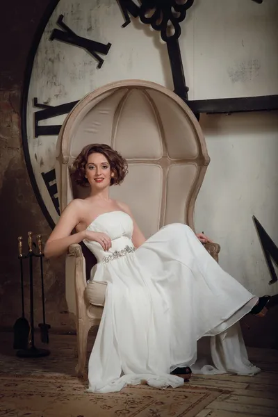 A noiva em uma cadeira no fundo de relógios e lareira conjunto de ferramentas. Tonificado vintage . — Fotografia de Stock