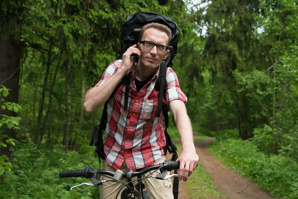 Mladý muž s kol mluví v lese na mobilním telefonu. — Stock fotografie