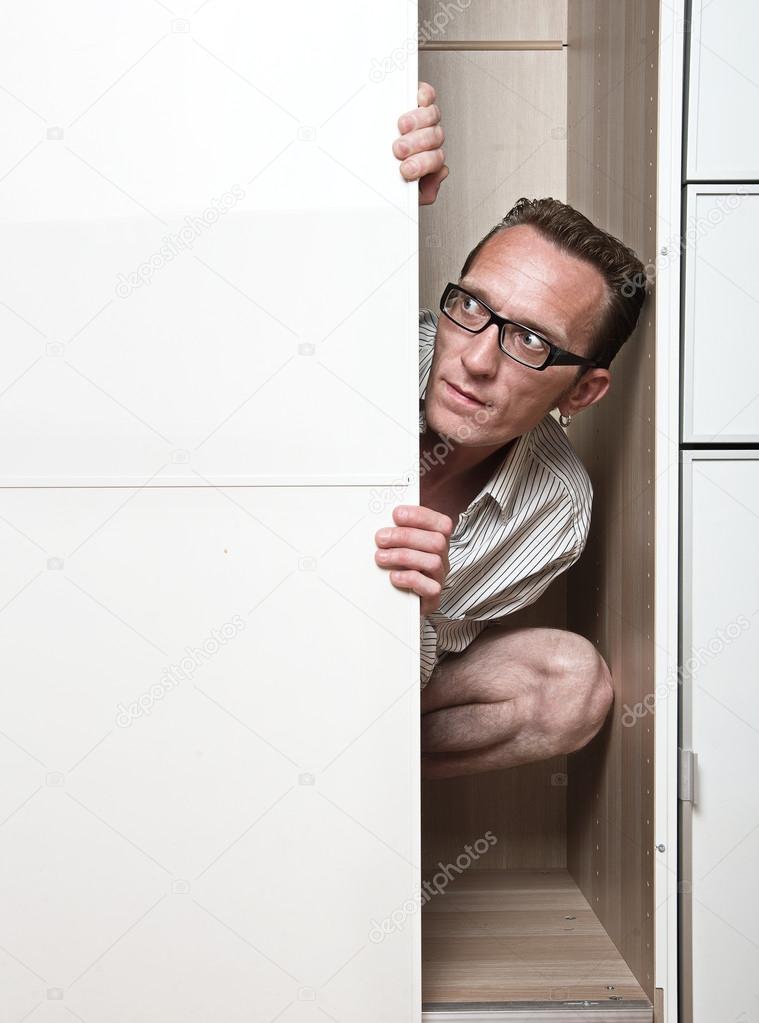 Prying man hiding inside white wardrobe