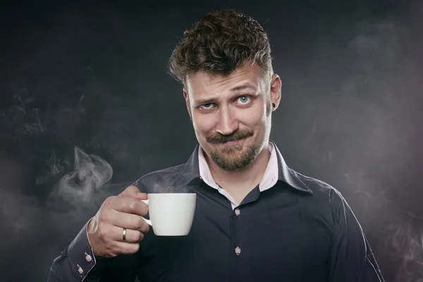 Hombre de barba guapo de pie en la niebla con una taza de café en la mano y mira a la cámara Imágenes de stock libres de derechos