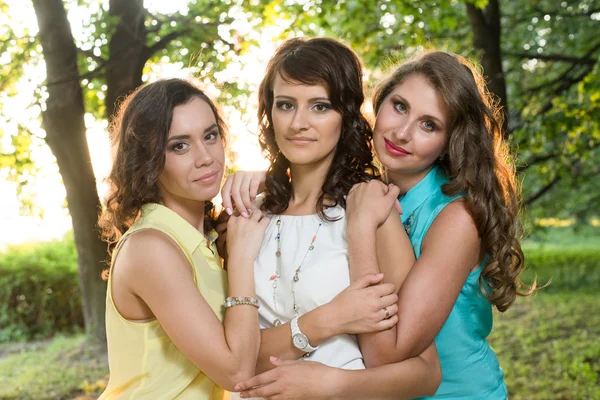 Trois jeunes belles dames posant lors d'une promenade dans le parc de la ville près de la rive de la rivière sur un coucher de soleil . — Photo