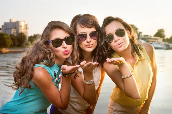 Drie stijlvolle vriendinnen in zonnebril verzenden lucht kus met camera. — Stockfoto