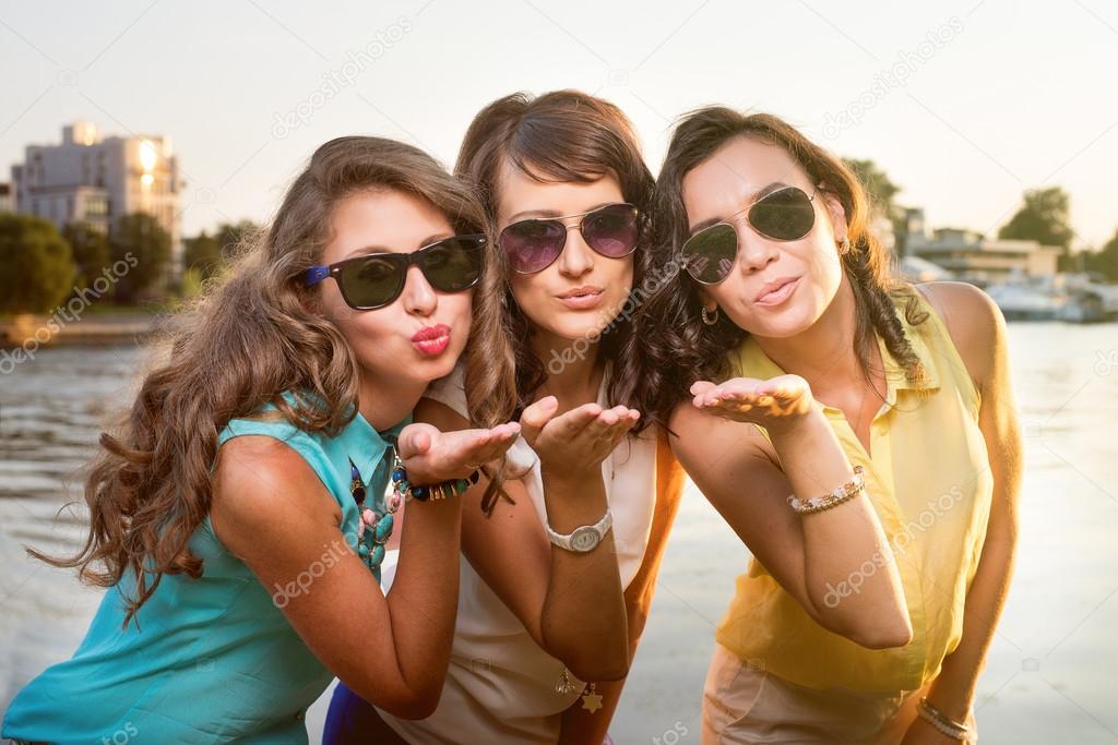 Three stylish girlfriends in sunglasses send air kiss to camera.