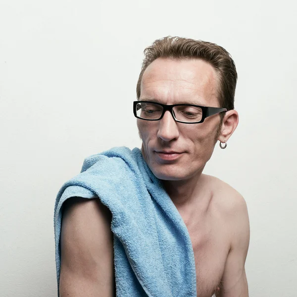 Pěkný nahý muž v brýlích s modrým ručníkem na rameni po koupeli, usmíval se a sedí na židli. — Stock fotografie