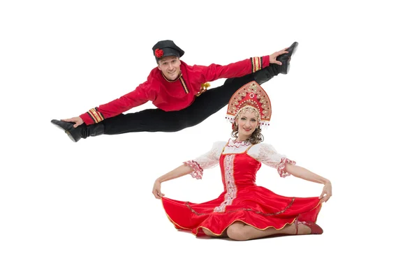 Pareja de bailarines en trajes tradicionales rusos, chica en sarafán rojo y kokoshnik, chico en pantalones negros y camisa roja Hombre hace un salto — Foto de Stock