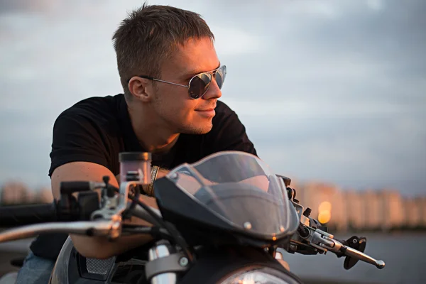 Muž motorkář na západu slunce blízko jezera a město — Stock fotografie