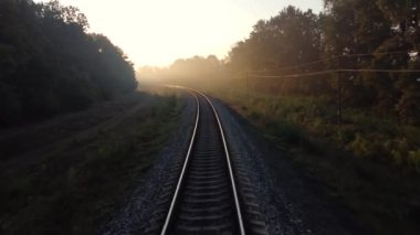 Tren yolu sabah sisi ile kaplı, güneş ışığı ağaç dalları ve uzun gölgeler arasında..