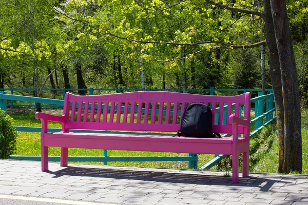 A pink bench in the park near the path. Rubzak on the bench under the tree