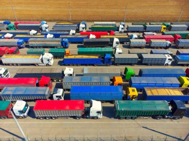 Aerial view of colorful trucks in terminal at sunset in summer. Top view of logistic center. Heavy industry. Transportation. Cargo transport, shipping. International trucking. View from drone of truck.