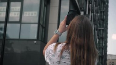 Genç kız bir kanal için video çekiyor. Yüksek yeni binanın videosu, sonra harabeler. Yaz günü, açık gökyüzü