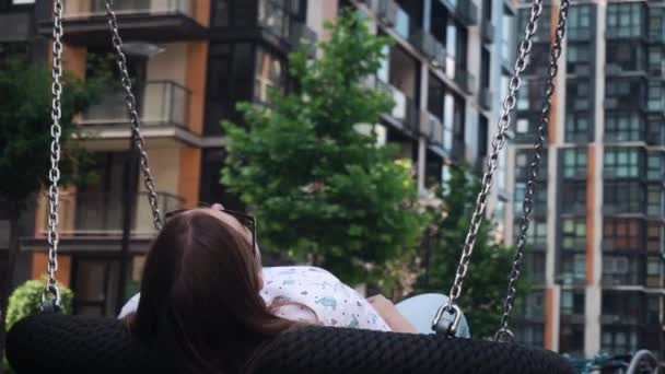 Menina com cabelo escuro relaxado em um balanço feito cordas e correntes, verão, dia claro. — Vídeo de Stock