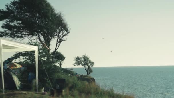 Вид на утренний кемпинг с большими зелеными деревьями на высокой когтистой скале у моря — стоковое видео
