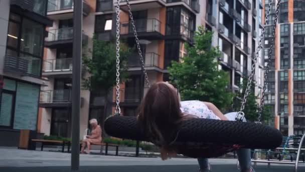 Meisje met donker haar ontspannen schommel gemaakt van touwen en kettingen, zomer, heldere dag. — Stockvideo