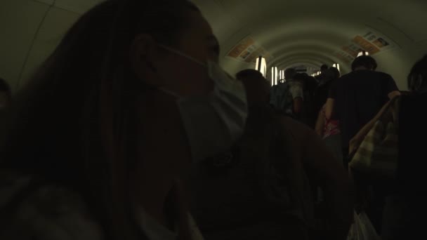 Cestující v lékařských maskách vyjíždějí po eskalátoru v metru během dopravní špičky — Stock video