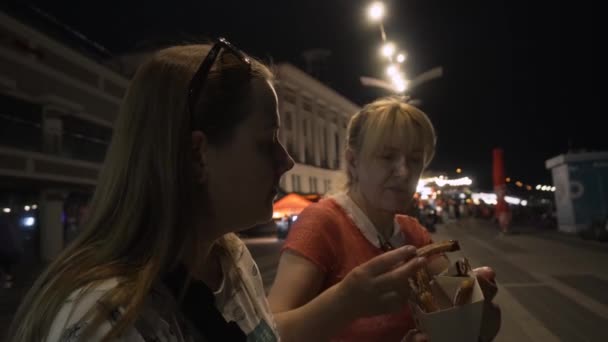 Women enjoy donuts with chocolate while sitting on the waterfront of the city — Stock Video