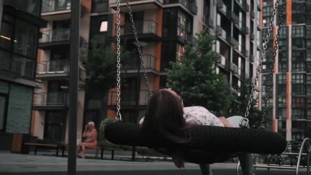 Dívka s tmavými vlasy uvolněná na houpačce z provazů a řetězů, léto, jasný den. — Stock video