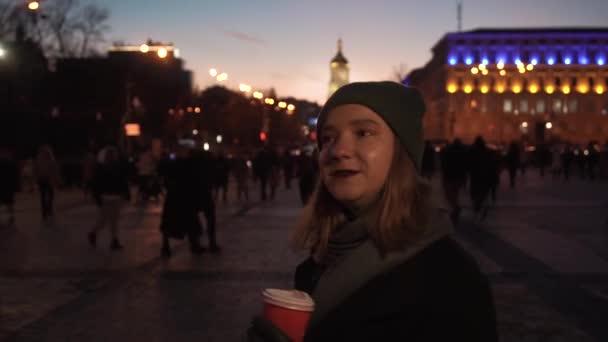Dziewczyna z kawą na głównym placu, w płonących światłach miasta, ferie zimowe — Wideo stockowe
