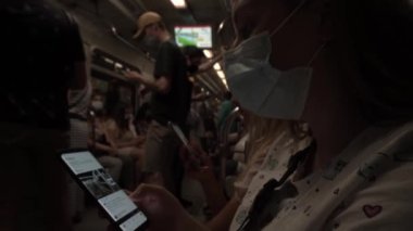 Genç kız sağlık maskesi, metro vagonu dolusu insan, sosyal mesafeyi gözlemeden.