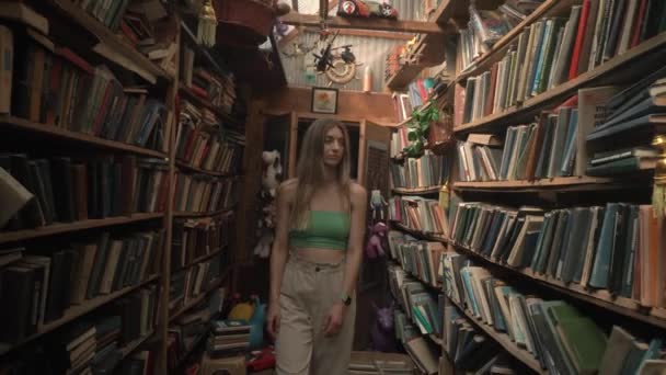 Rubia paseo abandonado, vieja biblioteca, entre estantes de madera con libros raros — Vídeos de Stock