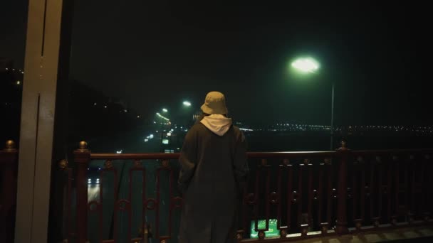 A girl stands on the bridge at night and looks at the lights of the big city — Stock Video