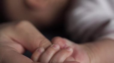 Bebek, annesinin elini küçük parmaklarıyla sıkıyor. Yakın plan.