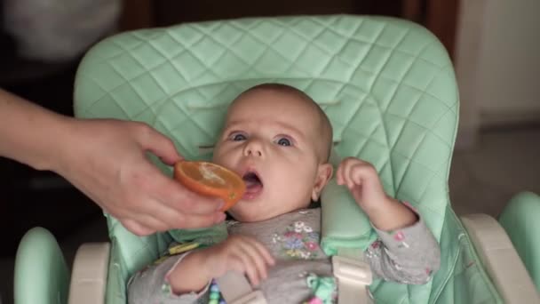 Un bebé con ojos azules se muestra una naranja. Bebé chupando sus dedos — Vídeos de Stock