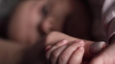 Bebek, annesinin elini küçük parmaklarıyla sıkıyor. Yakın plan.