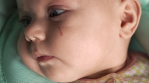 Närbild av ett barnansikte. Baby i barnstol tittar bort och framför kameran — Stockvideo