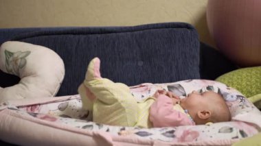 Memnun, mutlu küçük bebek, emer ellerini ve parmaklarını, seğirir, hareket ettirir bacaklarını, oynar, eğlenir