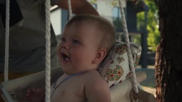 Daddy rides a little daughter on a swing. The child has a cross on his neck — Vídeo de Stock