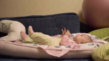 Neşeli küçük bebek, tek başına oynuyor, eğleniyor, odayı inceliyor. Çocuk tulumu giymiş bir çocuk, koza içinde bir yatağın üzerinde. Yan görünüm