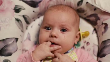 Büyük, mavi gözlere yakın çekim. Heyecanlı, tatmin olmuş, çocuk kostümü giymiş, ellerini ağzına koyan, çiçek desenli yataklı rahat bir koza. Kameraya bakıyor, parmaklarını deniyor, çiğniyor. Meme ucu. İyi akşamlar.