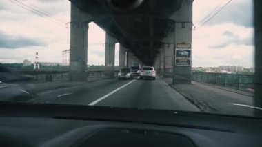 Arabanın ön camında bir çatlak var. Köprünün yollarındaki otomobil trafiği destek kuvvetleriyle, tren için. Yaklaşan araba trafiği. Nehir, ada, ağaçlar, bulutlu gökyüzü. Araç içi