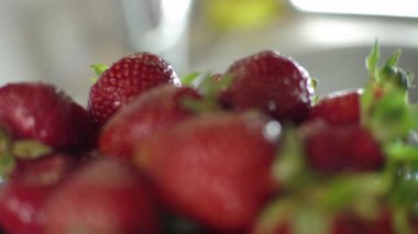 Kırmızı çilek dolu bir vazo. Yeşil yapraklar, küçük taneler. Makro. Kamera sürücüsü meyvenin üzerinde