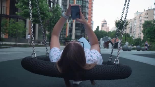 Girl Long Blond Hair Sunglasses Lies Swing Reads Messages Phone — стоковое видео