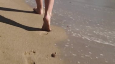 slender beautiful female legs walk along the wet warm sand on the Black Sea coast, leaving deep footprints. waves crashing, filming from behind, close-up