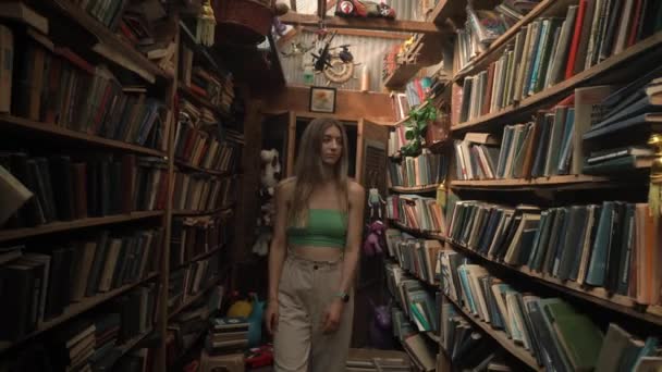 近代的で美しくスタイリッシュな女の子は 放棄された古い図書館を通って 珍しい本の木製の棚の間を歩きます 横に検討し 何を読むかを選択します — ストック動画
