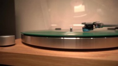 Medya oynatıcısına yeni yeşil müzik plakası yüklendi. Müzik bir iğneyle çalınır. Genel çekim, sarı lamba ışığı. Soldaki ses rölesi. Şeffaf kapak açık, iğneye odaklan