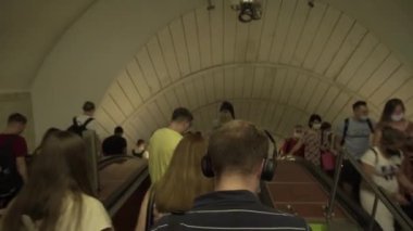 Kalabalık bölünmüş insanlar, karantinada metroya maskesiz, sosyal mesafeli gidiyorlar. Büyük avizeleri, korkulukları, kemerleri olan güzel metro istasyonu.