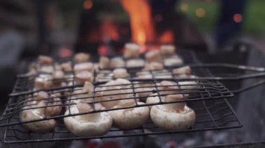 Yakın plan. Mantarlar tel askıda, sulu mantarlar ızgarada, kırsalda, yazın. Yeşil bir arka planda, ateş, alev, kıvılcım, kor, şenlik ateşi