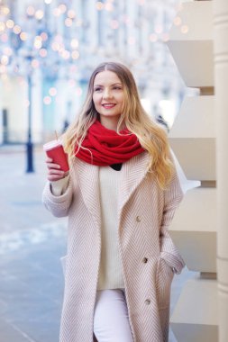 Kırmızı eşarplı mutlu sarışın kız kahve fincanı ile süslenmiş Noel alışveriş merkezinin arka planında yakın plan portresi