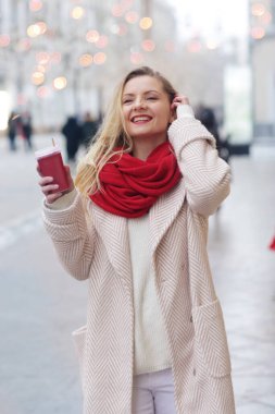 Kırmızı eşarplı mutlu sarışın kız kahve fincanı ile süslenmiş Noel alışveriş merkezinin arka planında yakın plan portresi