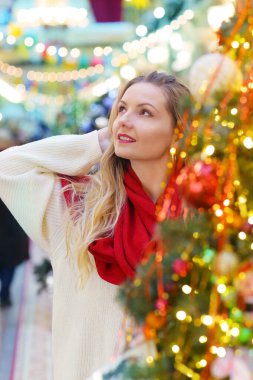 Kırmızı eşarplı mutlu sarışın kız dekore edilmiş Noel arkaplanındaki portreyi kapat.