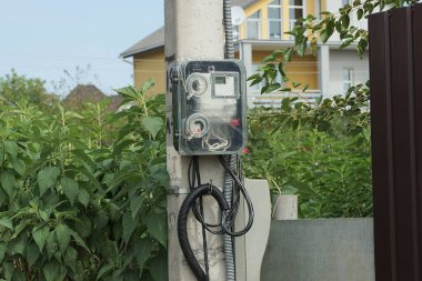 Bir gri plastik elektrik ve gaz sayacı sokağın yakınındaki beton bir direğe asılmış.