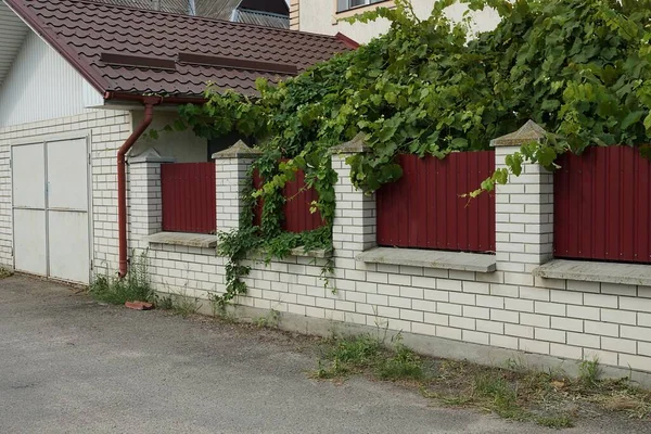 车库立面 墙上有灰色铁门 墙是用白色砖头和红色金属做成的 街道上有绿色的植被 — 图库照片