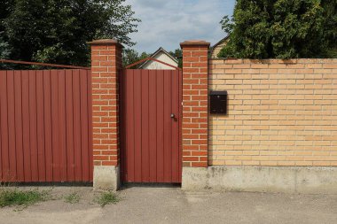 Kahverengi tuğlalı bir duvarda kırmızı kapalı metal bir kapı var.