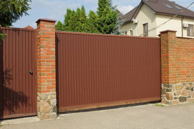 Kahverengi büyük metal kapı ve caddedeki kırmızı tuğla çitin kapalı kapısı.
