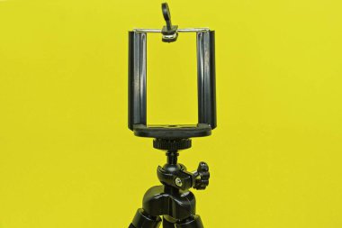 Sarı arka planda tripoda siyah bir akıllı telefon monte edilir.